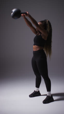 Vertical-Video-Full-Length-Studio-Shot-Of-Woman-Wearing-Gym-Fitness-Clothing-Exercising-With-Kettlebell-Weights